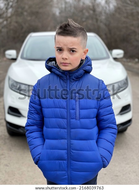 European guy stands in front of the car.Person\
standing next to an SUV.A young man stands in front of a white car\
waiting.