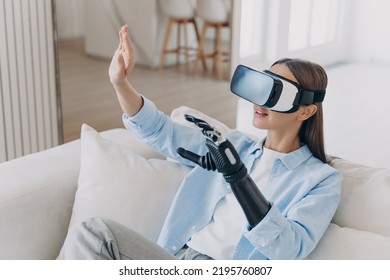 European Handicapped Girl In Vr Glasses On Sofa At Home. Disabled Person Gets Rehabilitation For Sensor Cyber Arm. Young Woman Is Playing Game. Healing Technology, Myoelectric Robotic Limb.