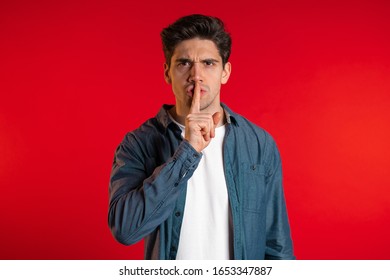 European Handsome Man Holding Finger On His Lips Over Red Background. Gesture Of Shhh, Secret, Silence