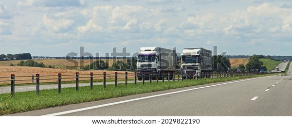 European heavy trucks into oncoming traffic\
lane on the countryside highway road motion at Sunny autumn day on\
yellow field and road lane fence background, goods delivery\
transportation\
logistics