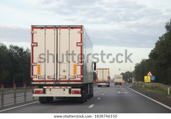 European heavy trucks with white semi trailers\
van drive on left side of two lane suburban asphalted highway road,\
back view at summer evening on forest and sky background,\
transportation\
logistics
