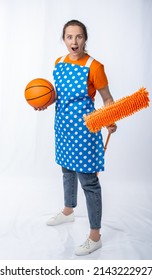 European Housewife In A Kitchen Apron, Jeans On A White Background, Full Length Portrait. Woman With A Mop And A Basketball. Fan Watching The Game At Home