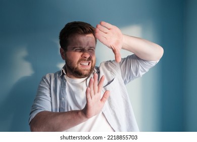 European man is annoyed by the sunlight, which blinds him. Blue background.