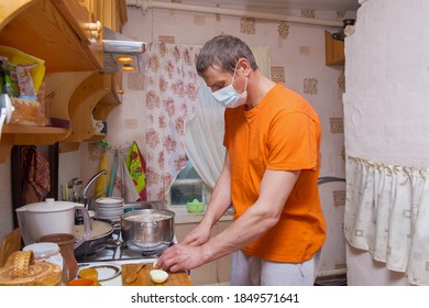 A European Man Is Engaged In Cooking In The Kitchen. A Man, 40 Years Old, Wearing A Medical Mask. Covid-19 Prevention Concept.