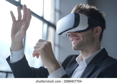 European man office employee wears formal suit and VR headset glasses excited of experiencing virtual reality stretching his hands up trying to catch seemingly round object totally immersed in 3D game - Powered by Shutterstock