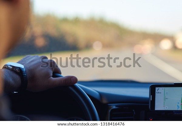 European man is searching
appropriate route while driving a car, he is using his smartphone.
Insight view.