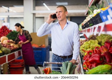 European Man Shopping In Greengrocer And Talking On Phone. Woman Merchandiser Working In Background. High Quality Photo