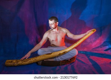 A European man sits and holds an ancient musical instrument didigeridoo in his hands.