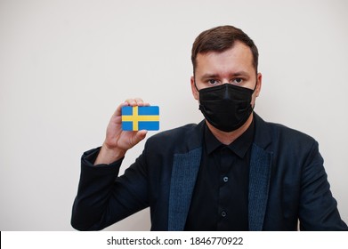 European Man Wear Black Formal And Protect Face Mask, Hold Sweden Flag Card Isolated On White Background. Europe Coronavirus Covid Country Concept.