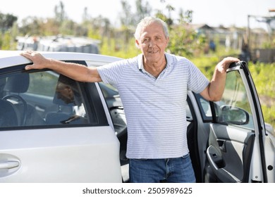 European mature man has arrived in village, comes out of car. Senior man visit country house and vegetable garden on bright sunny day. He stand next to open car door against background of vegetable - Powered by Shutterstock