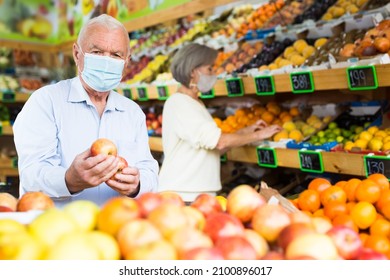 European old man in face masks choosing selecting apples in greengrocer. Mature woman standing behind and selecting fruits.