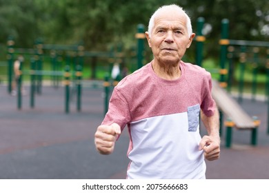 European Old Man Running Beside Playground In Urban Park.