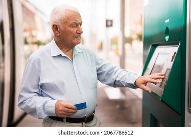 European Old Man Standing On Tram Stop And Using Cash Machine With Credit Card.