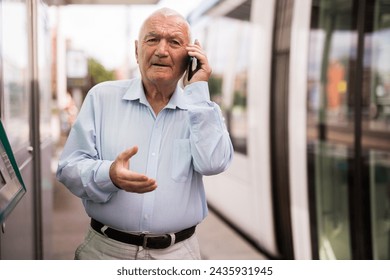 European old man standing on tram station and talking on phone. - Powered by Shutterstock