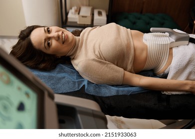 European pretty woman on daybed getting a non surgical body sculpting, body contouring treatment, anti-cellulite and anti-fat therapy on a lipo laser in beauty salon. Hardware cosmetology concept