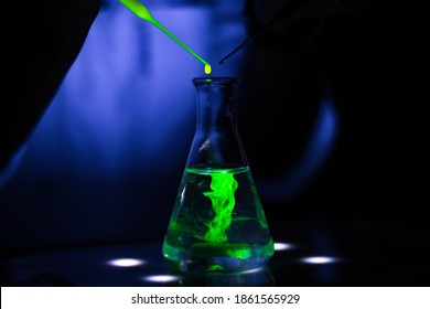  European researcher working with a green fluorescent compound in dark chemistry laboratory for pharmaceutical development