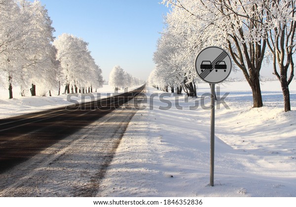 European road sign END ZONE OVERTAKING\
PROHIBITED on roadside on white snowy trees after snowfall\
background at Sunny winter day, winter road driving\
safety