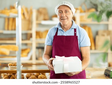 European senior man entrepreneur owner of bakery holds out cardboard box with pastries in hand, ready to meet buyer and sell goods. Seller presenting product in box with bow decoration - Powered by Shutterstock