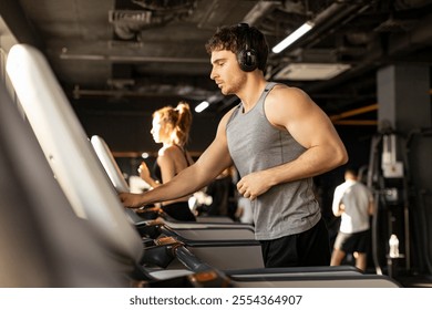 European sportsman adjusting speed on treadmill while running, working out and listening music in gym interior - Powered by Shutterstock