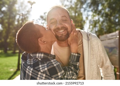 European teenage boy with cerebral palsy hugging and kissing happy adult father in sunny park. Family relationship and enjoy time together. Disability care and rehabilitation. Fatherhood and parenting
