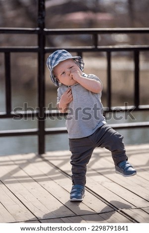 
European toddler child in a panama hat sucks his thumb and makes unsteady steps on the terrace in spring