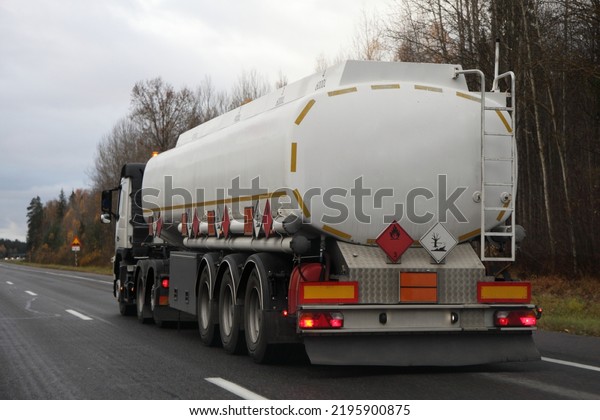 European tree-axle semi truck fuel tanker move on\
suburban highway road at autumn evening in perspective, back side\
view, gasoline fuel ADR dangerous cargo transportation logistics in\
Europe