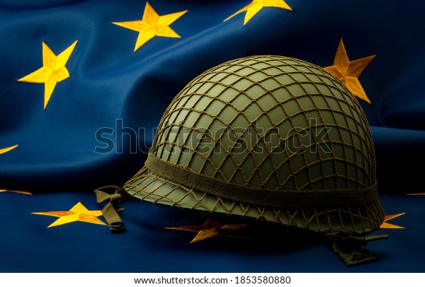 European union army, military uniform and\
defense of Europe concept with soldier helmet with camouflage\
pattern and the EU flag in the\
background