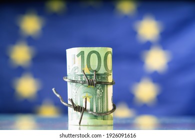 European Union Currency Wrapped In Barbed Wire Against Flag Of EU As Symbol Of Economic Warfare, Sanctions And Embargo Busting.