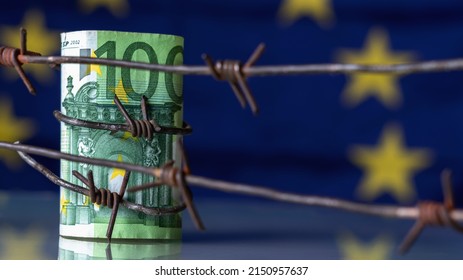 European Union Currency Wrapped In Barbed Wire Against Flag Of EU As Symbol Of Economic Warfare, Sanctions And Embargo Busting. Horizontal Image. Copy Space.