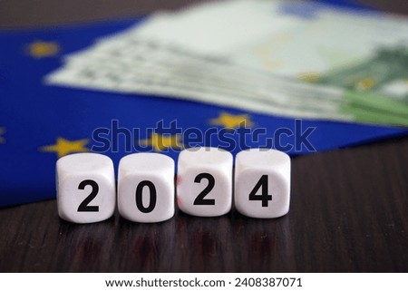 european union flag, cubes with 2024 and big stcak of euro money on wooden table, European parliamen elections June 9, 2024, concept, closeup