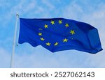 The European Union flag waves as it is prominently displayed, fluttering in the breeze against a bright blue sky, symbolizing unity and cooperation among European nations.