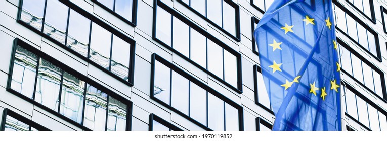European Union flag waving in front of modern corporate office building, symbol of EU Parliament, Commission and Council. - Shutterstock ID 1970119852