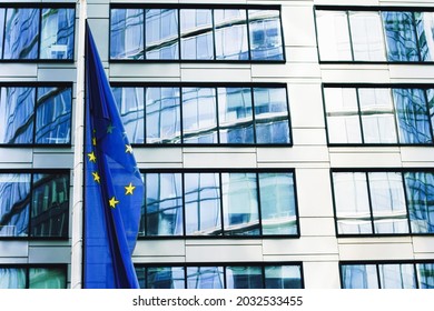 European Union flag waving in front of modern corporate office building, symbol of EU Parliament, Commission and Council.