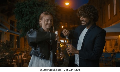 European woman and Arabian Indian Latino man open bottle of beer cider clink glasses walk street outside city evening friends drinking smiling weekend multiracial couple celebrate happy together enjoy - Powered by Shutterstock