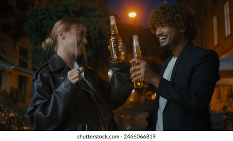 European woman and Arabian Indian Latino man open bottle of beer cider clink glasses walk street outside city evening friends drinking smiling weekend multiracial couple celebrate happy together enjoy - Powered by Shutterstock