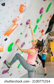 European woman grabbing ledges of artificial climbing wall in bouldering centre. - Shutterstock ID 2130771314