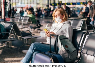 A European Woman In A Protective Medical Mask On Her Face Sits At The Airport Waiting For A Flight And Uses The Phone.