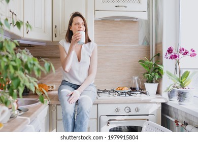 a European woman sits on the table in her kitchen and drinks coffee, breakfast in the kitchen coffee and croissant, internet detox and rest in the morning, calm and measured breakfast, rest and time - Powered by Shutterstock