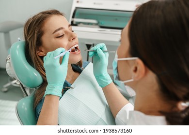 European young woman sitting in medical chair while dentist fixing her teeth at dental clinic - Powered by Shutterstock