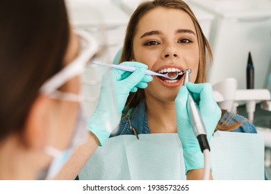 European Young Woman Sitting In Medical Chair While Dentist Fixing Her Teeth At Dental Clinic