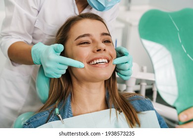 Joven europea sonriendo mientras mira el espejo en la clínica dental