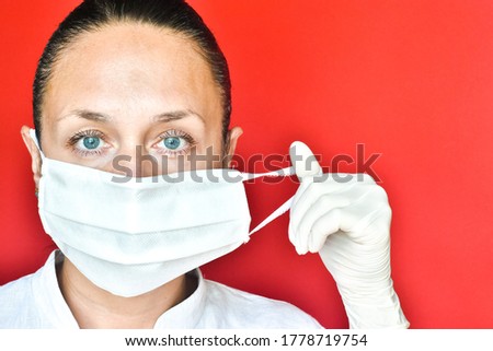 European young woman takes off her medical mask in latex gloves talking on the phone on a red background. space for text, close-up. healthcare concept, medicine.