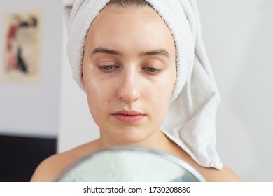 Eurpean blonde woman with glowing skin looking into mirror with towel wrapped around her head against white background. Close-up. Morning routine. - Shutterstock ID 1730208880