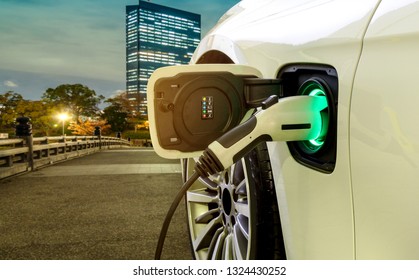 EV Car Or Electric Car At Charging Station With The Power Cable Supply Plugged In On Blurred Night Cityscape Background.	