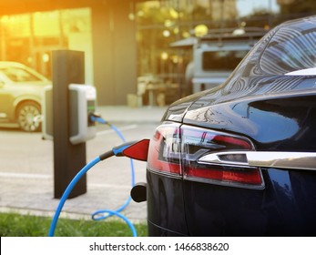 EV Car Or Electric Car At Charging Station With The Power Cable Supply Plugged In On Blurred City Background