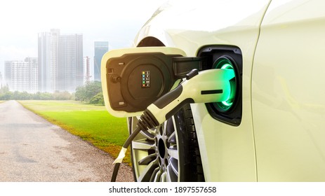EV Car or Electric car at charging station with the power cable supply plugged in on Green environment with a long road leading to the city of the future.