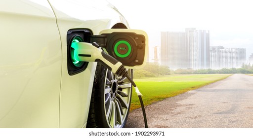 EV Car or Electric car at charging station with the power cable supply plugged in on Green environment with a long road leading to the city of the future.	