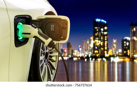 EV Car or Electric car at charging station with the power cable supply plugged in on blurred Night cityscape background.