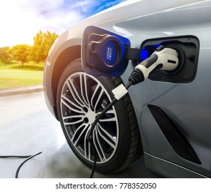 EV Car or Electric car at charging station with the power cable supply plugged in on blurred nature with sun light background. Eco-friendly alternative energy concept