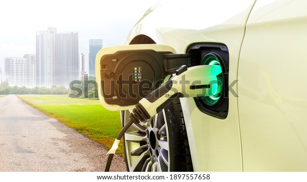 EV Car or Electric car at charging\
station with the power cable supply plugged in on Green environment\
with a long road leading to the city of the\
future.